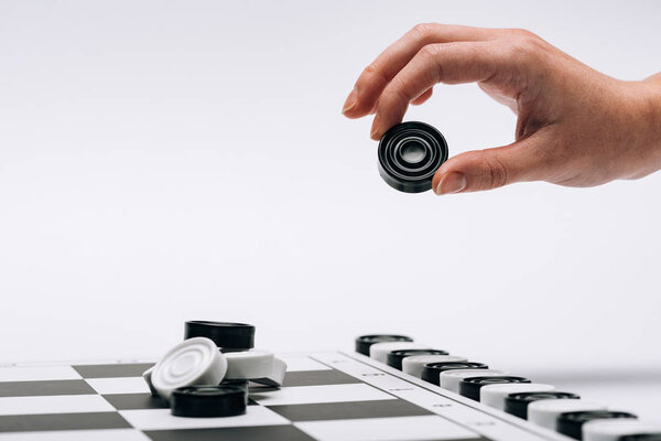 Обрезанный вид женщины, держащей черную шашку с шашечной доской, изолированной на белом
