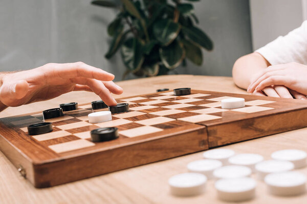 Cropped view of man and woman playing checkers won wooden checkerboard at table