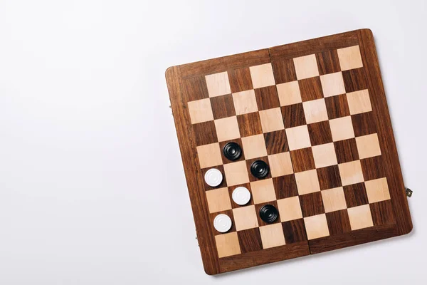 Top view of checkers on wooden checkerboard on white background