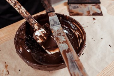 selective focus of cake scrapers near bowl with melted dark chocolate  clipart