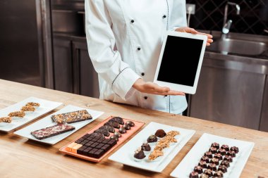 Tabaklarda çikolatalı şekerlerin yanında boş ekran bulunan dijital tablet tutarken çikolatacı görüntüsü. 
