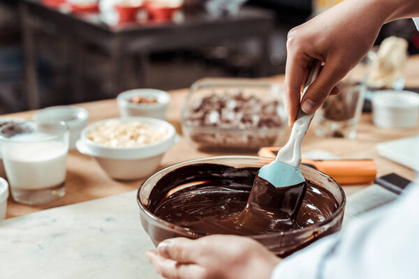 cropped view of chocolatier holding silicone spatula while mixing chocolate in bowl 