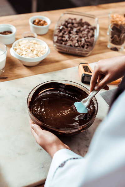selective focus of chocolatier holding silicone spatula while mixing chocolate in bowl 
