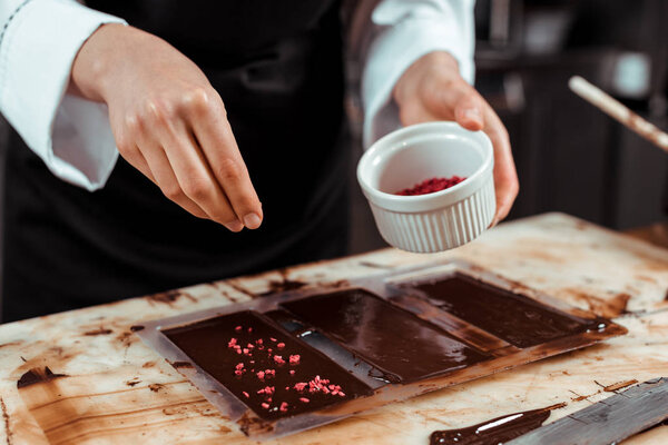 cropped view of chocolatier adding dried raspberries in chocolate bar 