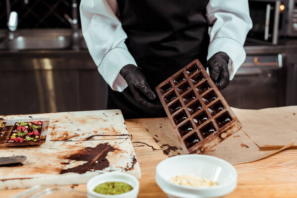cropped view of chocolatier holding chocolate molds near baking paper