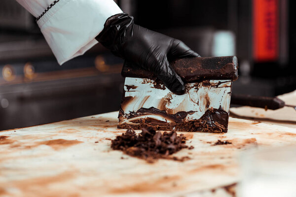 cropped view of chocolatier in black latex glove scraping dark chocolate from surface 