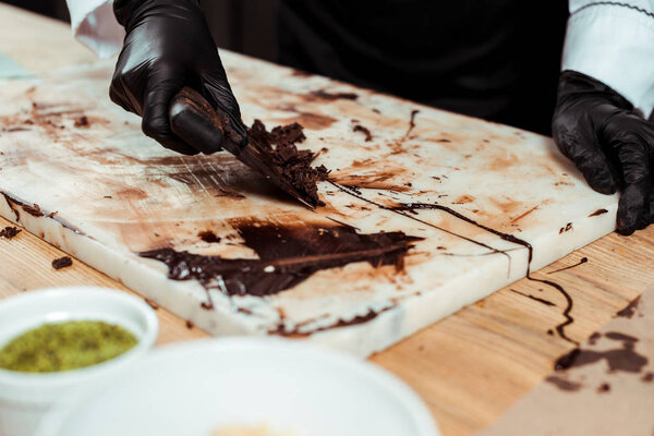 cropped view of chocolatier in black latex gloves scraping dark chocolate shavings 