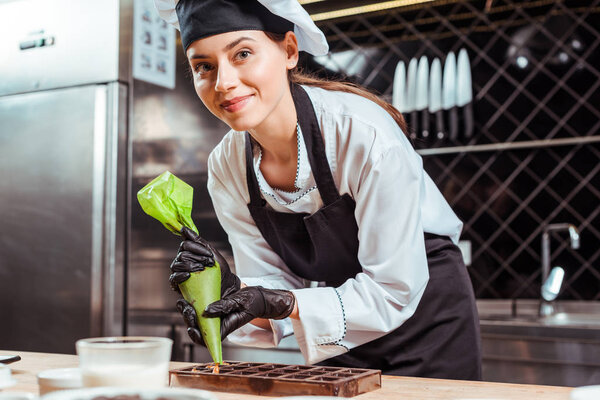 selective focus of happy chocolatier in black latex gloves holding pastry bag near chocolate molds 