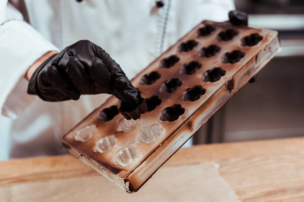 cropped view of chocolatier holding chocolate candy near ice tray 