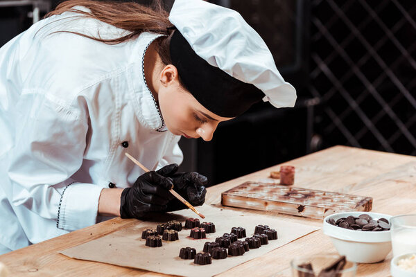 attractive chocolatier holding brush with gold powder near prepared chocolate candies 