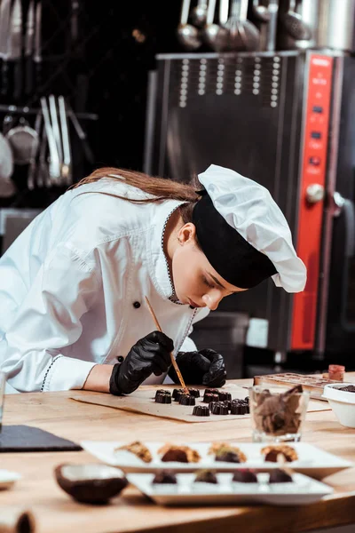 Çekici çikolata fırçasının seçici odak noktası. Yanında altın tozu bulunan fırça hazır çikolata şekerleri ve kabartma kağıdı. 