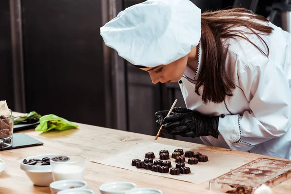 Belo Chocolatier Chapéu Chef Segurando Escova Com Ouro Perto Doces — Fotografia de Stock