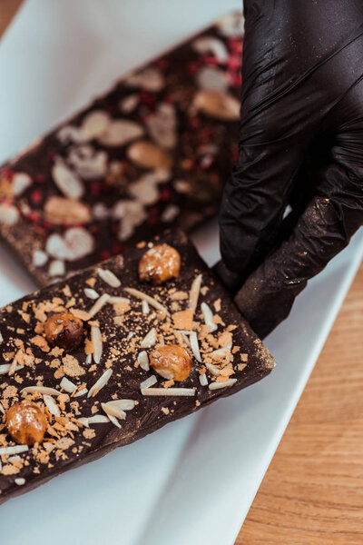 close up of chocolatier putting chocolate bar with hazelnuts on plate 