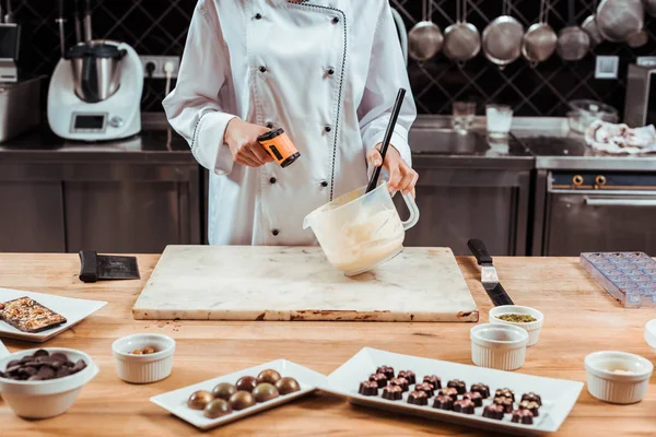 cropped view of chocolatier holding cooking thermometer near bowl with melted white chocolate