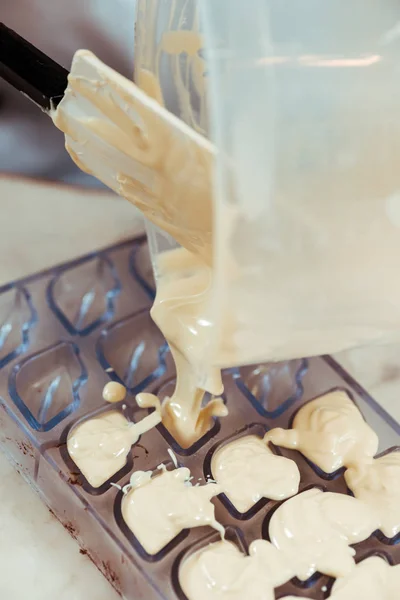 selective focus of silicone spatula near jug with melted white chocolate and chocolate molds