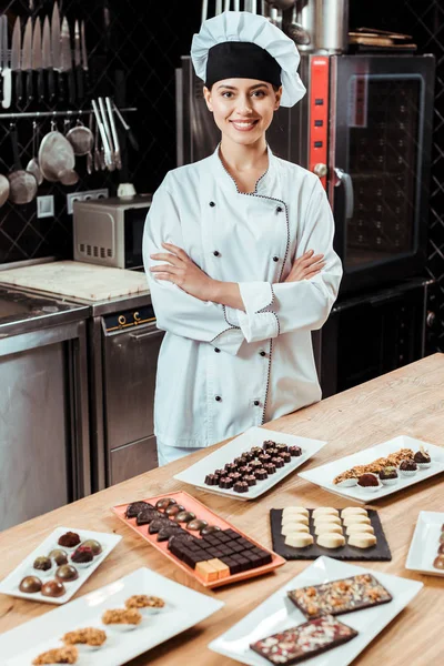 Sorrindo Chocolatier Com Braços Cruzados Perto Doces Chocolate Saborosos Placas — Fotografia de Stock
