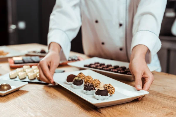 Cropped View Chocolatier Touching Plate Sweet Fresh Chocolate Candies — Stock Photo, Image