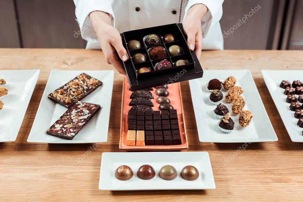 cropped view of chocolatier holding box with fresh made chocolate candies 