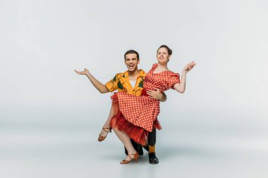 Yakışıklı dansçı, gri arka planda dans ederken, dizlerinin üzerinde duruyor ve partnerini destekliyor.