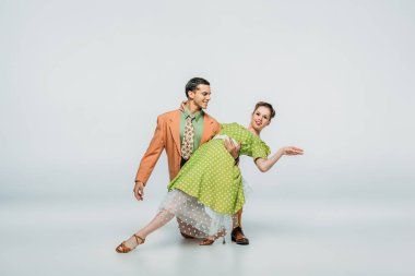 Yakışıklı dansçı, gri arka planda dans ederken, dizlerinin üzerinde duruyor ve partnerini destekliyor.