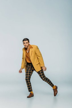 Yakışıklı, zarif dansçı, gri arka planda dans ederken kameraya bakıyor.