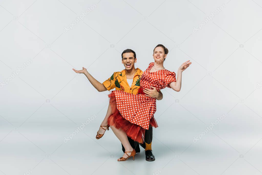 handsome dancer standing on knee and supporting partner while dancing boogie-woogie on grey background