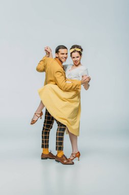 Gri arka planda dans ederken gülümseyen dansçılar el ele tutuşur.