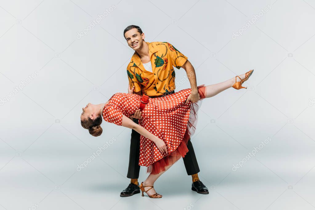 cheerful man supporting woman while dancing boogie-woogie on grey background