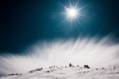 malebný pohled na hory pokryté sněhem a borovicemi proti tmavé obloze s bílým mrakem a sluncem