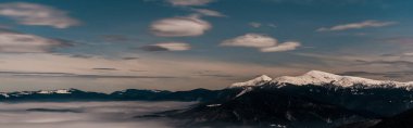 Akşamları beyaz kabarık bulutlu karlı dağların manzarası, panoramik çekim.