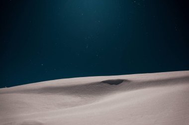 Gece yıldızlı gökyüzüne karşı bembeyaz karla kaplı dağların manzarası.