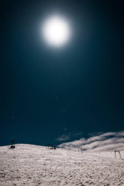 Karla kaplı dağdaki gondol manzarası parlayan güneşli karanlık gökyüzüne karşı