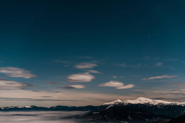 scenic view of snowy mountains with white fluffy clouds in evening