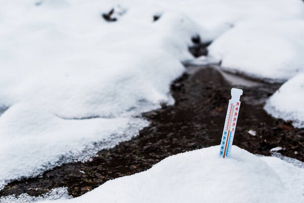 thermometer on snow near flowing mountain stream