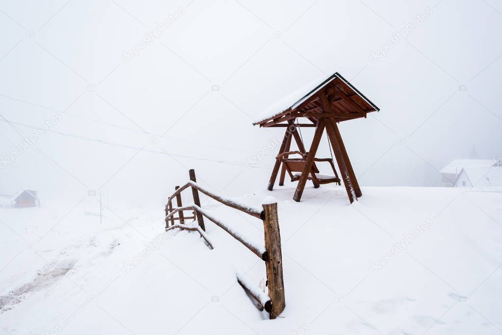 wooden fence and swing in snowy mountain village in fog