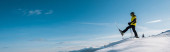 panoramatický záběr lyžaře držícího lyžařské hole a krok proti modré obloze v horách 