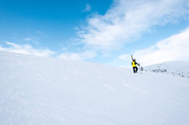 Kasklı kayakçı kışın yamaçta kayak sopalarıyla yürüyor. 