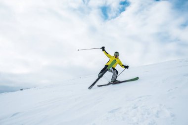 Heyecanlı sporcu elinde sopalarla beyaz yamaçta kayak yapıyor.