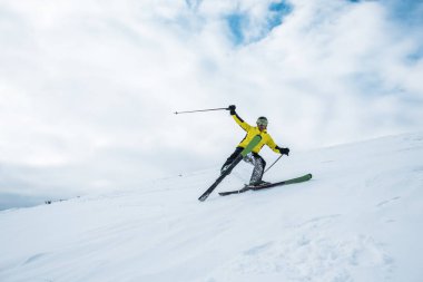 excited sportsman holding ski sticks and skiing on white slope clipart