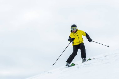 Kışın kasklı kayakçı elinde sopalarla yamaçta kayak yapıyor. 