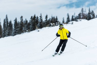 Kasklı kayakçı elinde sopalarla dağlarda yamaçta kayak yapıyor. 