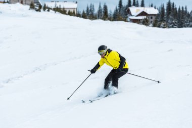 Kasklı kayakçı elinde sopalarla dağlarda karla yamaçta kayak yapıyor. 
