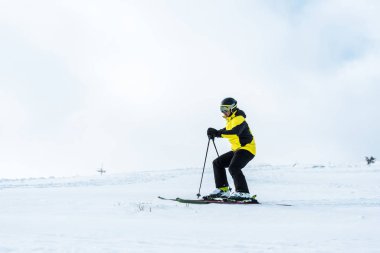 Kasklı sporcu elinde sopalarla yamaçta karla kayak yapıyor.