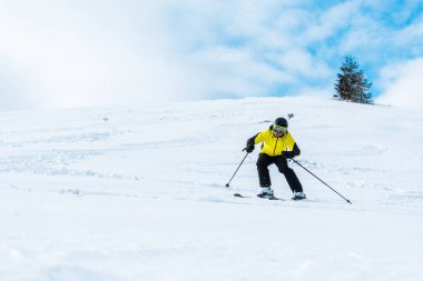 Kasklı sporcu gökyüzünde bulutlarla birlikte yamaçta kayak yapıyor. 
