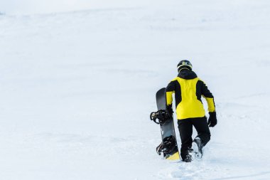 Kar üzerinde yürürken elinde snowboard tutan sporcunun arka görüntüsü 