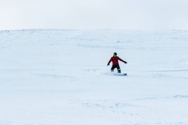 Kasklı snowboardcu dışarıda beyaz karla yamaçta geziyor. 
