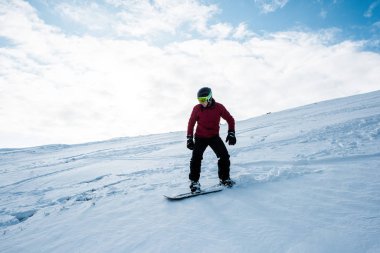 Kışın mavi gökyüzüne karşı yamaçta uçan miğferli snowboardcu. 
