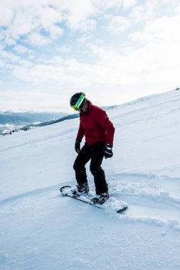 Kışın beyaz karla yamaçta uçan kasklı snowboardcu. 