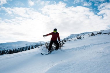 Gözlüklü ve kasklı snowboardcu kışın yamaçta geziyor. 