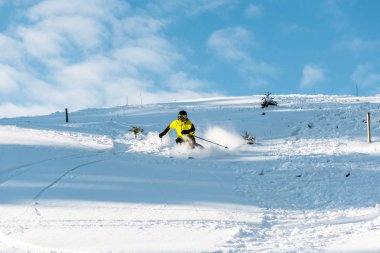Kasklı sporcu dışarıda yamaçta kayak yaparken elinde çubuklar tutuyor. 
